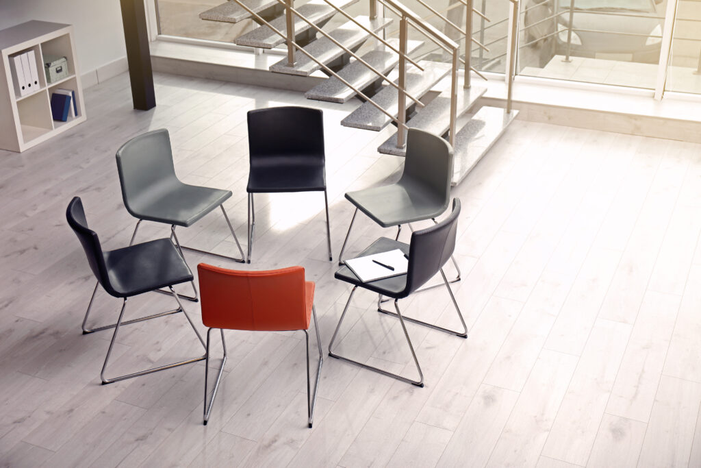 A small circle of chairs in a bright room with large windows, set for a group session