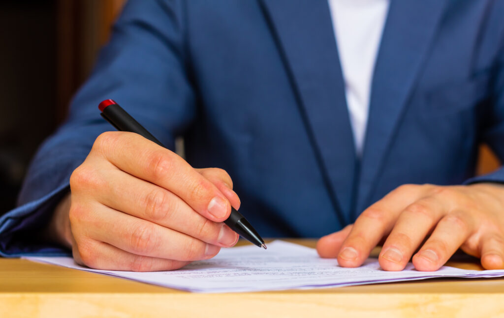 A person in a suit signing a document at a desk