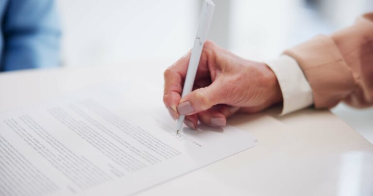 Close-up of a person's hands signing a printed document with a pen